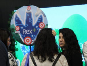 Asistentes conversando frente al stand de Rex+ en el congreso People Experience 2025 en Chile.